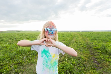 Children, festival of holi and holidays concept - happy little girl covered with color powder smiling over nature backgroundの写真素材