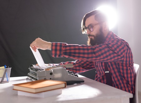 People and technology concept - World day of the writer, handsome man with beard working on typewriter over black backgroundの写真素材