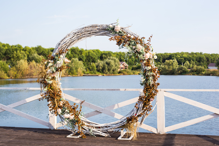 Area of the wedding ceremony in forest, near river on the pier. Wooden round arch. Cute, trendy rustic decorの写真素材