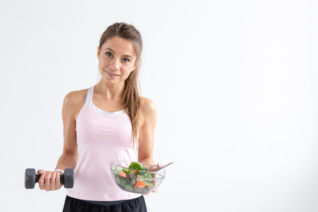 Healthy lifestyle, people concept - a plate of salad in one hand and dumbbell in another hand. Smile and fitness suitの写真素材