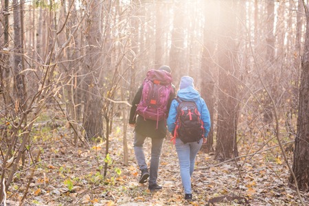 adventure, travel, tourism, hike and people concept - back view of couple walking with backpacks over autumn natural backgroundの写真素材