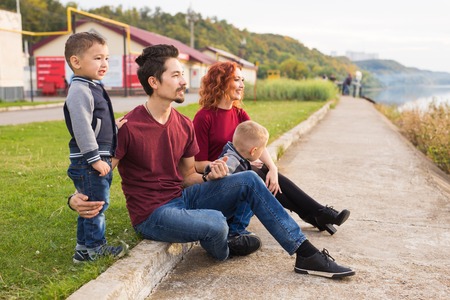 Parenthood, childhood and nature concept - Family sitting on the green ground and looking at small boatの写真素材