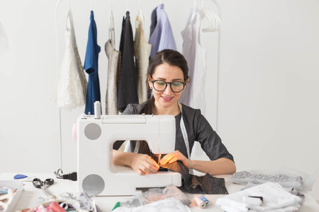 People, tailor, dressmaker and fashion concept - Smiling female fashion designer using sewing machineの写真素材