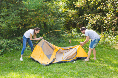 Young happy couple are preparing for camping. Theyre installing a tent on a suitable place in a meadow.の写真素材