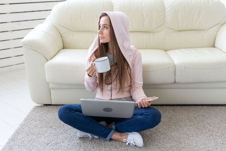 Technologies, freelance and people concept - young woman working at home, she is drinking tea on the floor, chatting in mobileの写真素材