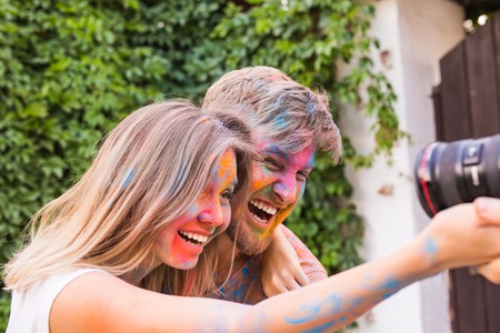 Holiday, holi and people concept - Woman and man with painted faces taking selfie over bush backgrundの写真素材