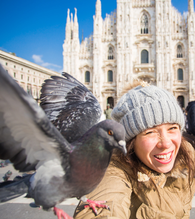Travel, holidays and winter vacations concept - Happy young woman take selfie photo with funny pigeons in front of Duomo Milan Cathedralの写真素材