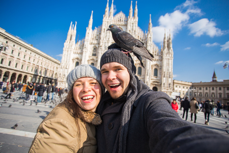 Winter travel and vacations concept - Happy tourists taking a self portrait with funny pigeons in front of Duomo cathedral in Milanの写真素材
