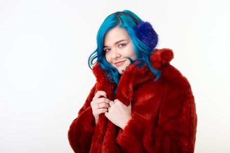 Animal protection, fashion and hair concept - beautiful girl wearing artificial fur coat with blue hair standing on white backgroundの写真素材