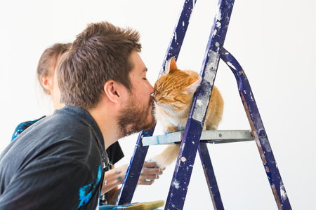 Repair, renovation, pet and love couple concept - young man with cat doing repair and painting wallsの写真素材