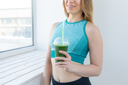 Healthy, fitness and detox concept - close up of young woman in sports wear with green smoothie smiling indoorsの写真素材