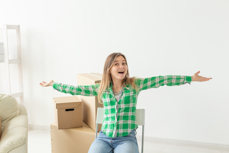 Charming young woman in casual clothes rejoices sitting on a chair among the boxes of things in her living room in a new apartment during the moveの写真素材