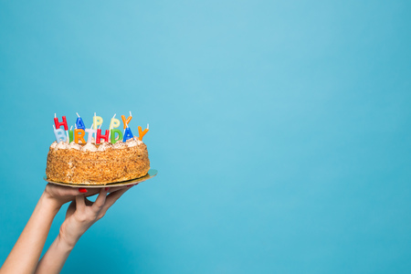 Hands holding a birthday cake with candles and the inscription birthday on a blue background. Congratulations on the anniversary and birthday. Copyspaceの写真素材