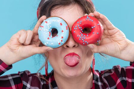 Diet, dessert and junk food - close up of pin-up pretty woman with doughnuts showing you a tongue on...