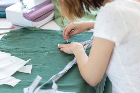 Hands of a young girl designer makes marks for a new sew product sitting at the table next to the...