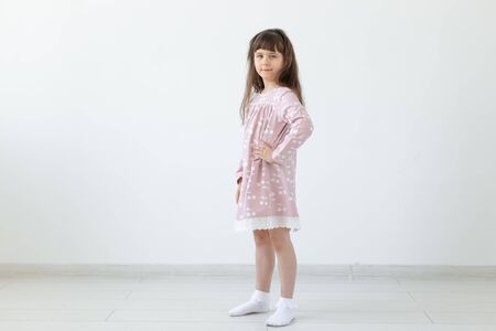 Little proud brunette girl in a pink dress is standing on a white background. The concept of stylish childrens clothing and preschool age. Copyspace.の写真素材