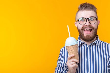 Hipster joyful crazy young guy holding a cocktail in his hands with a straw tube posing on a yellow background. Concept of cafes and restaurants. Advertising space.の写真素材