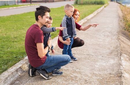 Parenthood, childhood and family concept - Parents and two male children walking at the park and looking on somethingの写真素材