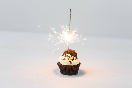 Food, party and holiday concept - Birthday cupcake with sparkler over white backgroundの写真素材