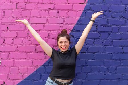 Cheerful positive young woman in goth clothing posing against a blue-purple brick wall. The concept...