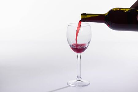 Red wine pouring into glass from bottle on white background with copy spaceの写真素材