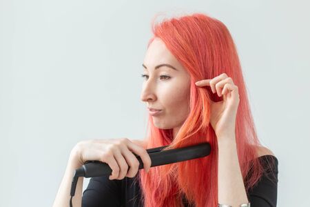 Style, fashion, hairdresser and people concept - stylish red-haired woman with curling iron on white...