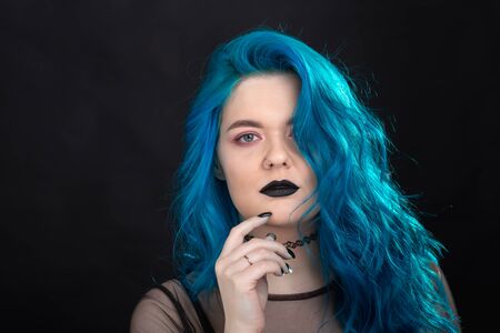 People and fashion concept - Young and attractive woman with black lipstick and blue hair posing over black backgroundの写真素材