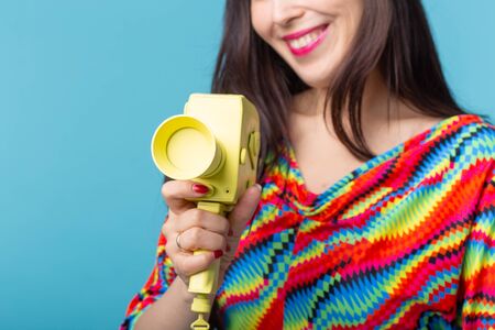 Beautiful positive young brunette woman holding in her hands a model of a yellow camcorder posing on...