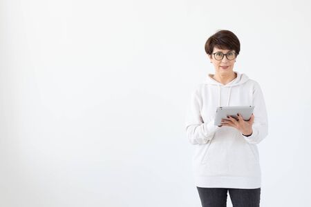 Cute middle-aged woman in casual clothes is looking online stores using a tablet on a white background. Concept of wireless internet and online shopping. Copyspace.の写真素材