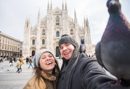 Winter travel and vacations concept - Happy tourists taking a self portrait with funny pigeons in front of Duomo cathedral in Milanの写真素材