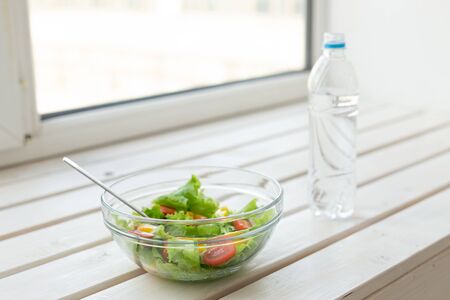 Vegetable salad and bottle of water lie on a white windowsill. Concept of healthy lifestyle physical activity and proper nutrition.の写真素材