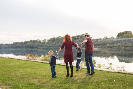 Parenthood and nature concept -Family of mother and father with two boys twins kids in a park at summer by a river at sunny dayの写真素材