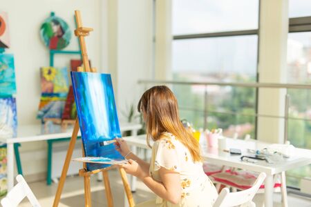 Art class, drawing and creativity concept - Female student sitting in front of easel with palette and paintbrushの写真素材