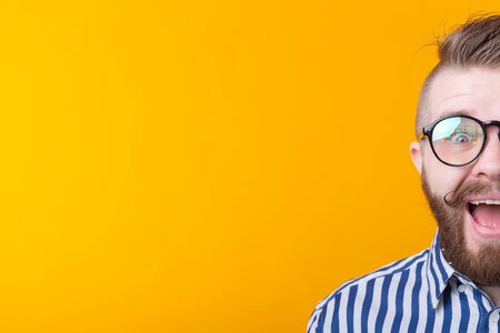 Stylish young hipster man with a mustache and beard joyfully opens his mouth on a yellow background with copy space. Concept of surprise and celebration.の写真素材