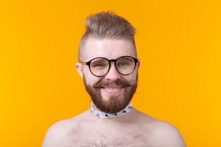 Young positive trendy man hipster with a mustache beard and fetish necklace in shirt posing on a yellow background. Concept of rock and subculture.の写真素材
