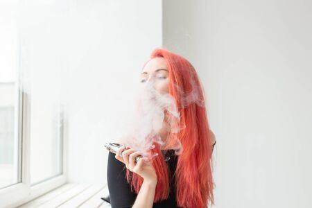 Vape, addiction and people concept - young woman with colored hair is smoking a vapeの写真素材