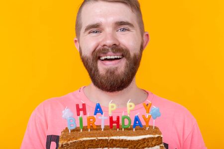 Crazy funny positive guy hipster holding a happy birthday cake in his hands standing on a yellow...