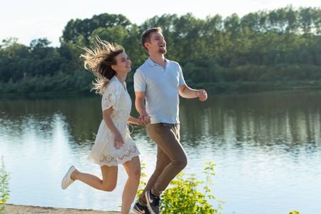 Summer nature, relationship and people in love concept - happy couple running near the lakeの写真素材