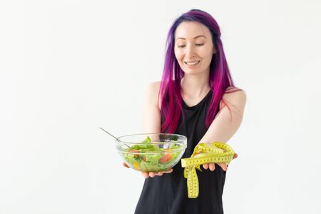 Young asian girl hipster colored hair holding in hands a measuring tape and vegetable salad posing on a white background with copyspace. Healthy eating concept.の写真素材