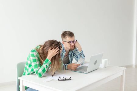 Young husband and wife are upset about numerous checks for payments and purchases for repairs while sitting at the table with a laptop. The concept of low living standards and savings.の写真素材