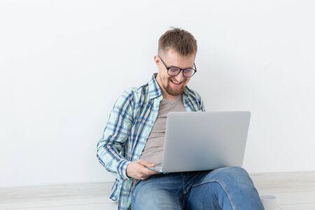 Positive young man in casual clothes and glasses surfing the Internet using WiFi and a laptop in...