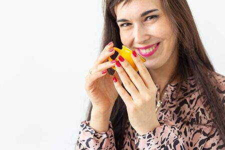 Playful young brunette woman holding in her hands a small yellow mug posing on a white background. Concept of morning coffee.の写真素材