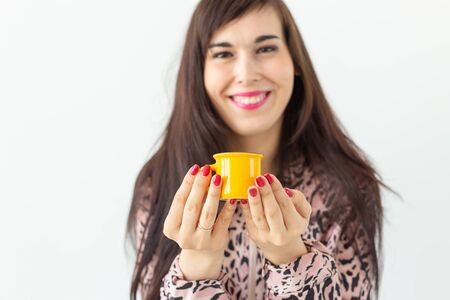 Cute young woman holding a small toy yellow mug in her hands posing on a white background. Favorite drinks conceptの写真素材