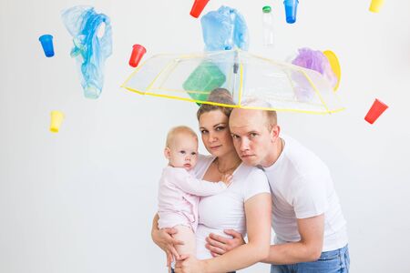 World Environment Day, plastic recycling problem and environmental disaster concept - Sad family hiding from garbage under an umbrella on white backgroundの写真素材