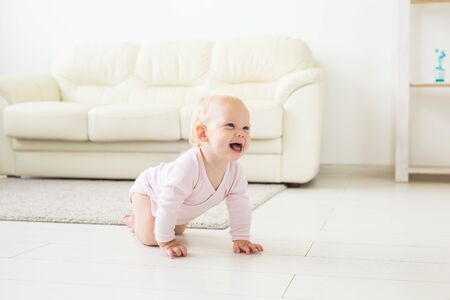 Adorable baby girl learning to crawl in white sunny room.