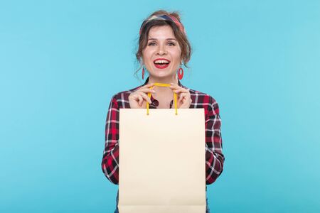 Happy young beautiful woman in a plaid shirt and jeans and holding a bag on a blue background....