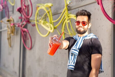 Cute stylish arab young male hipster with a mustache and a beard and wearing glasses drinking juice with a straw. Summer vacation concept.の写真素材