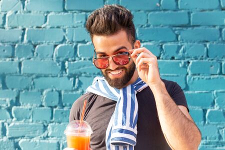 Cute stylish arab young male hipster with a mustache and a beard and wearing glasses drinking juice with a straw. Summer vacation concept.の写真素材