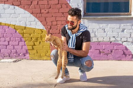 Handsome man is holding and hugging cute cat outdoorsの写真素材