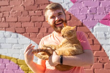 Handsome man is holding and hugging cute cat outdoorsの写真素材